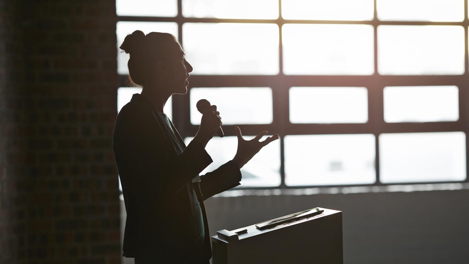 silhouetted woman at a podium microphone