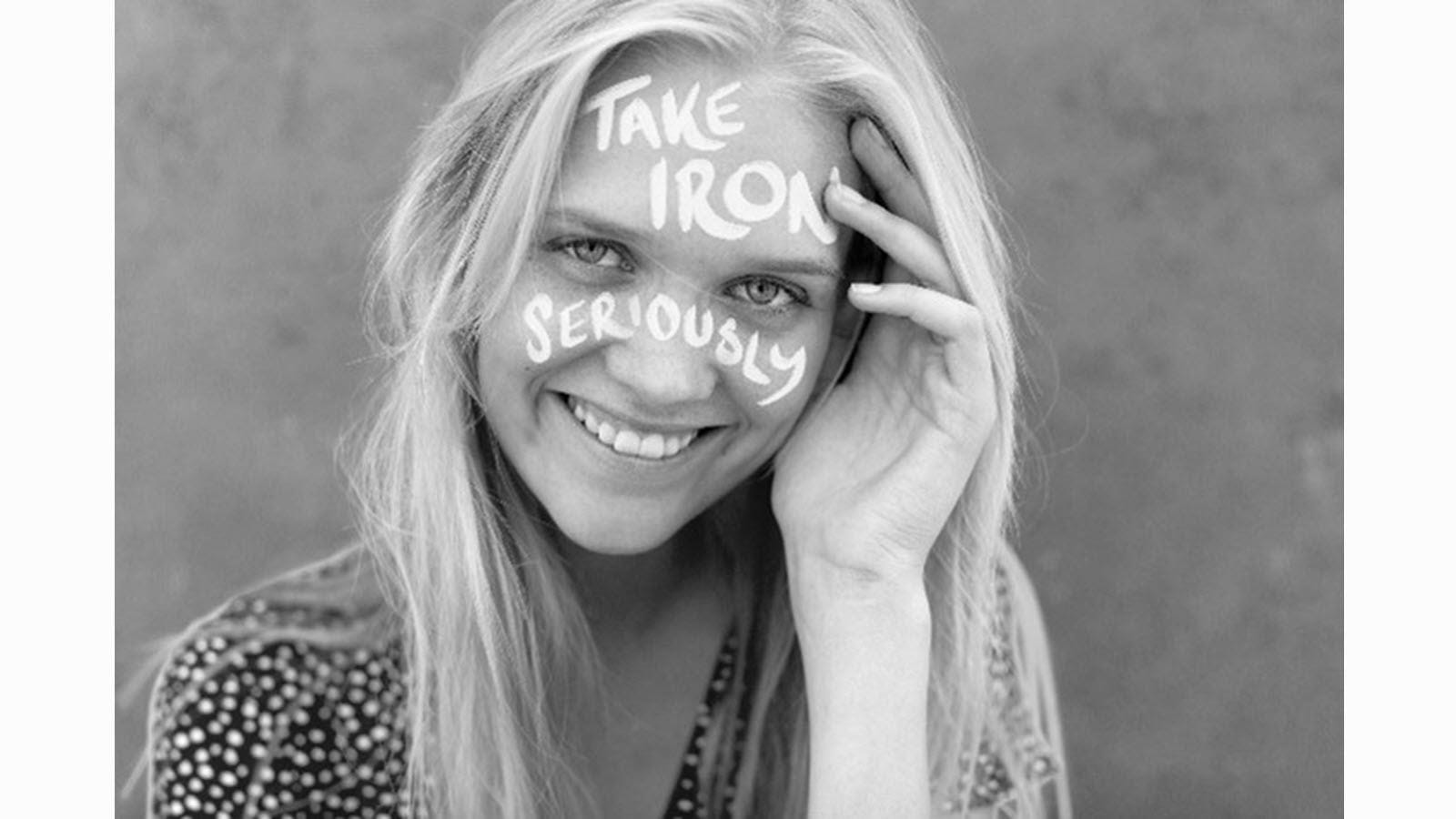 Young woman with white writing on her face that says take iron seriously