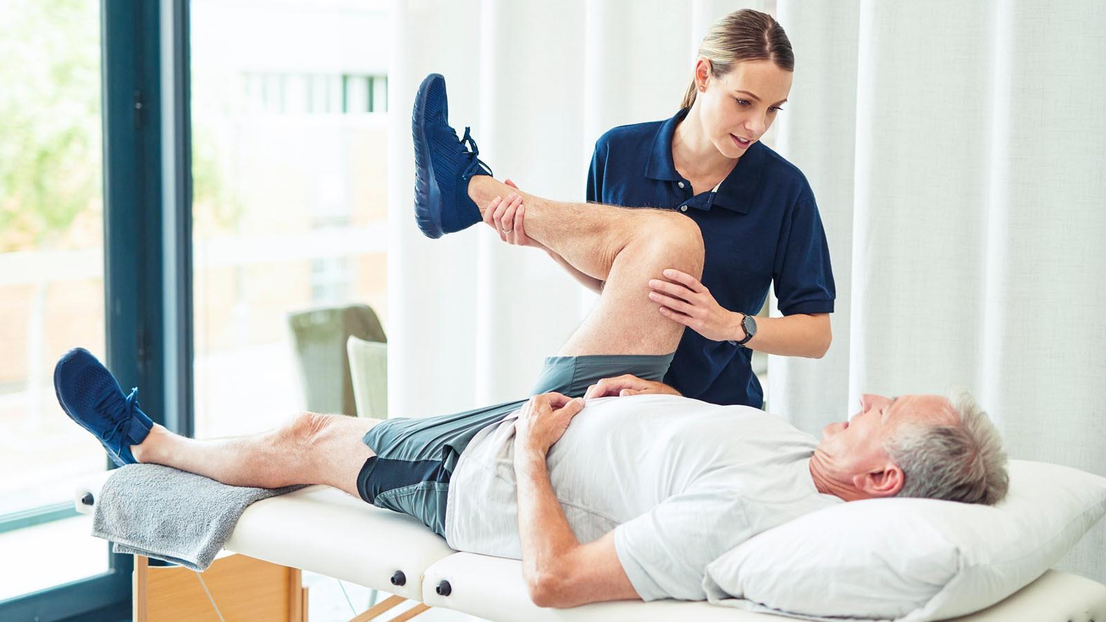 A physical therapist helps a patient with a leg exercise