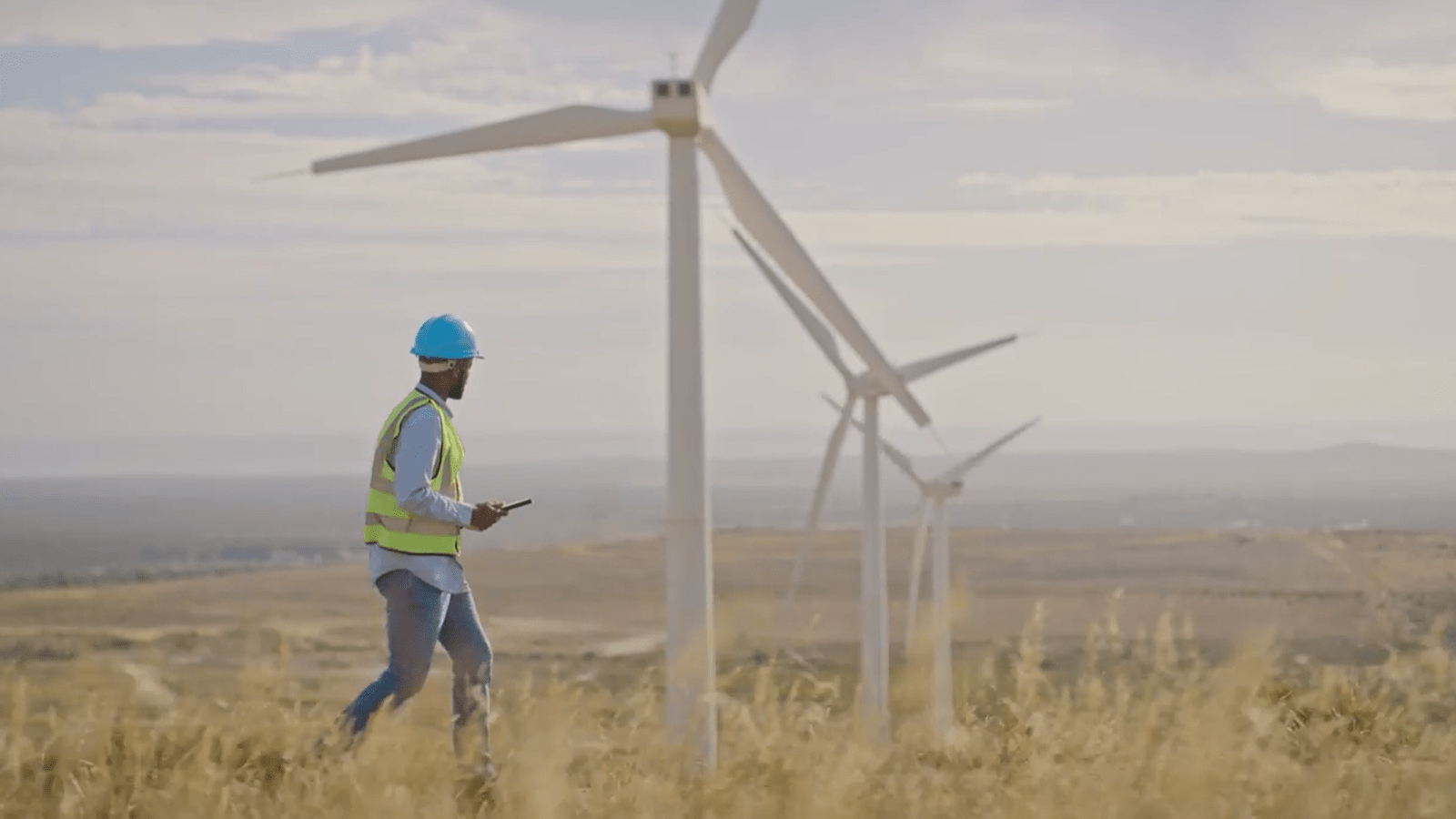 Utility worker walks in a field of wind turbines.