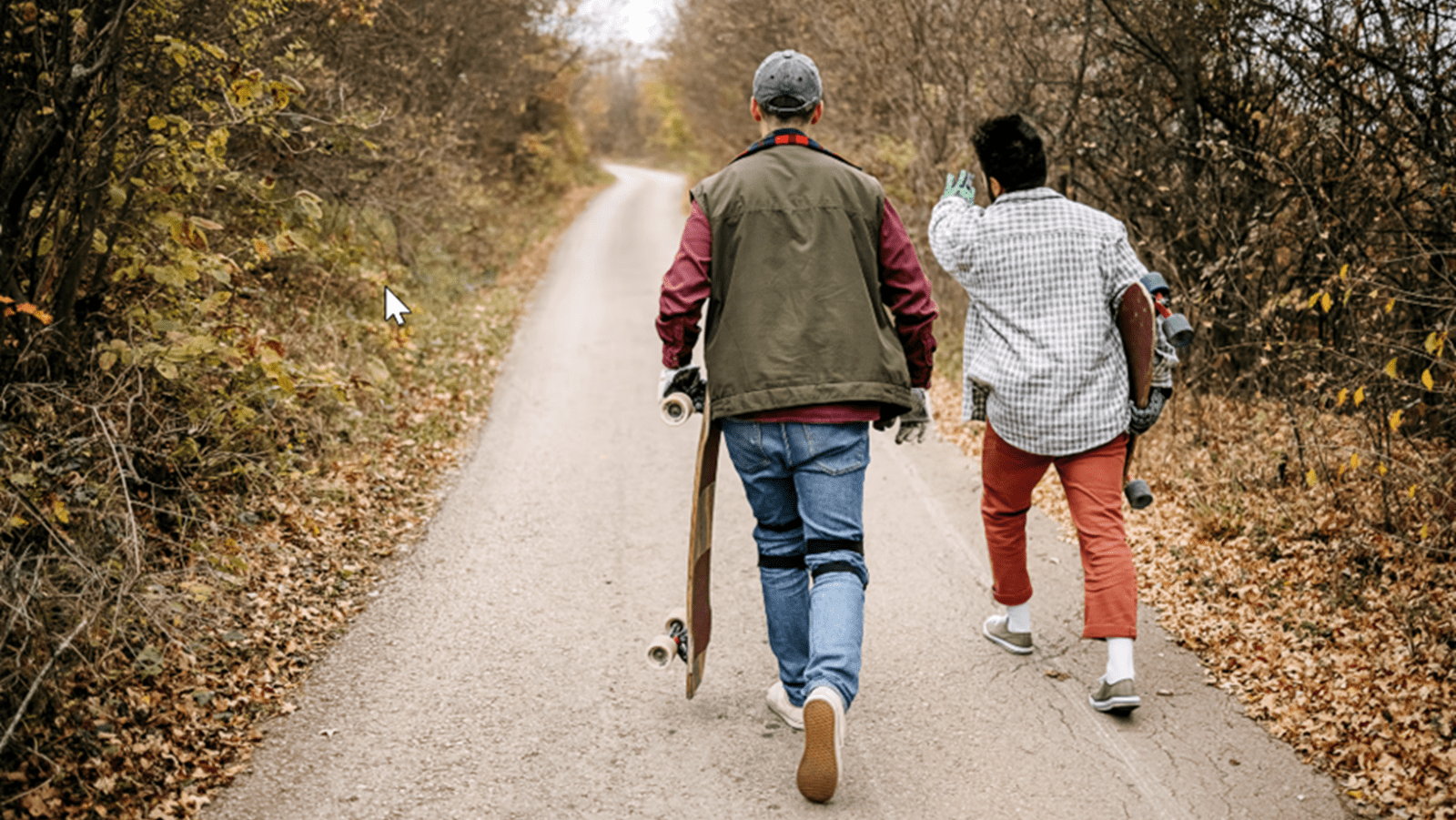 Two skateboarders walk down a path in autumn
