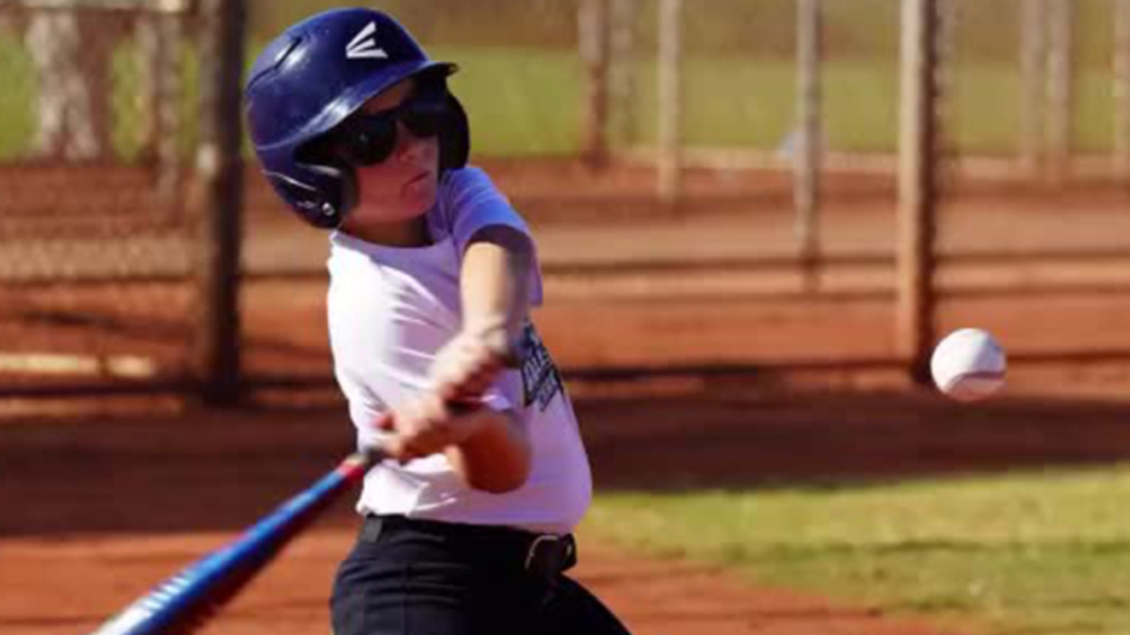 Young baseball player in sunglasses swings a baseball bat.
